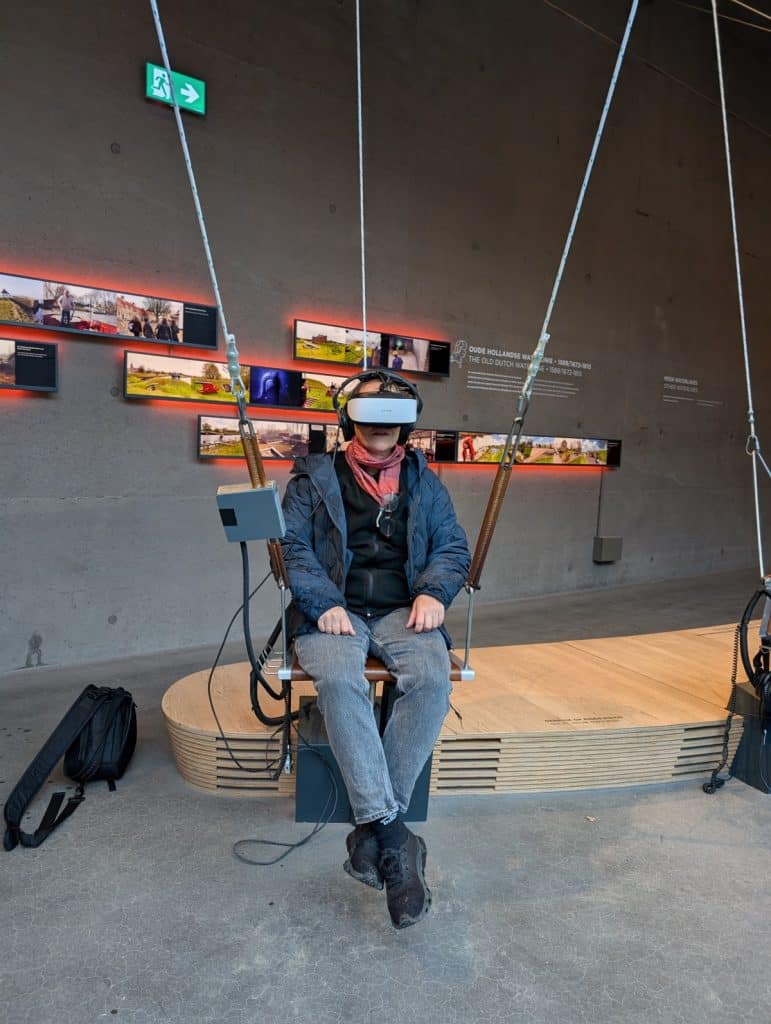 Eine Person sitzt im Waterlinie Museum bei Utrecht auf einer schaukelähnlichen Vorrichtung und trägt ein VR-Headset für eine virtuelle Flugsimulation.