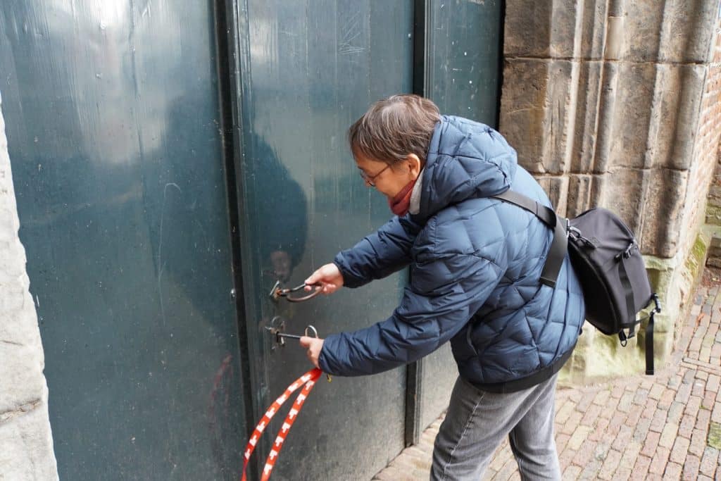 Eine Person in einer blauen Steppjacke öffnet mit zwei großen, historischen Schlüsseln die schwere Eingangstür einer Kirche in Wijk bij Duurstede.