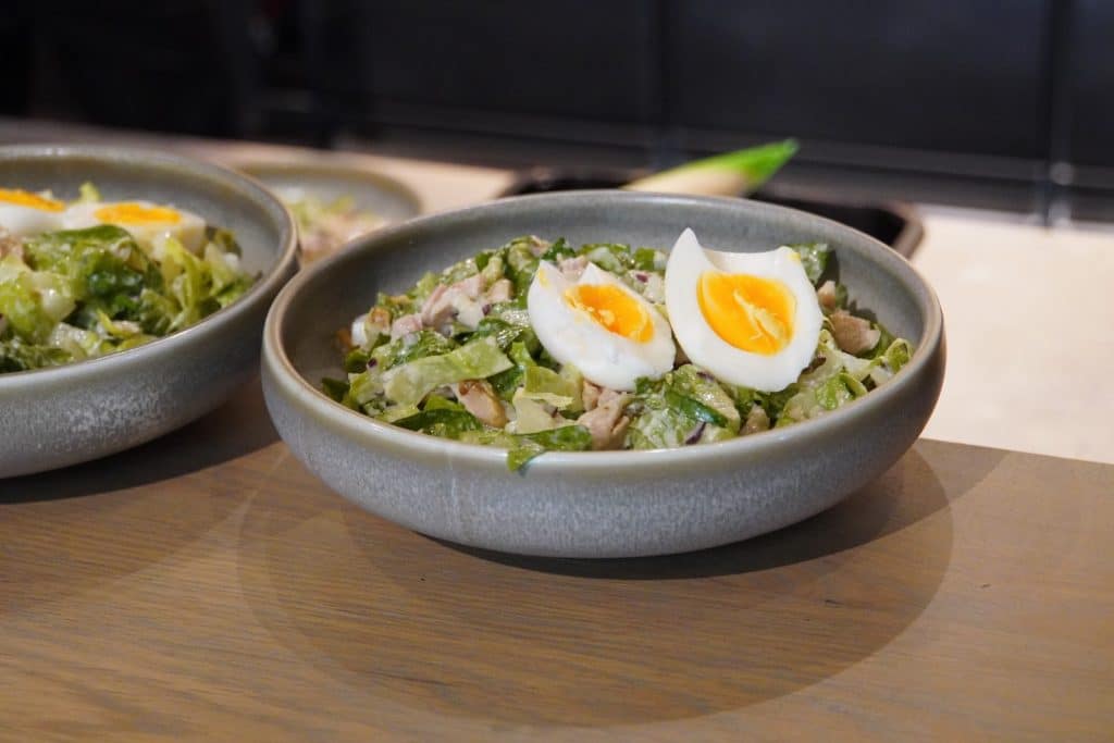 Zwei Schalen mit frischem Salat garniert mit halbierten, wachsweich gekochten Eiern, stehen auf einer Holzoberfläche.