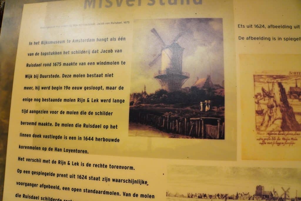 Eine Informationstafel mit dem Titel „Misverstand“ zeigt ein historisches Gemälde der Windmühle von Jacob van Ruisdael sowie begleitende niederländische Texte zur Geschichte des Bauwerks.