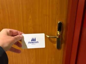 Eine Hand hält eine weiße Zimmerkarte des Maritim Hotels Hannover vor eine hölzerne Hotelzimmertür mit goldfarbenem Türgriff.