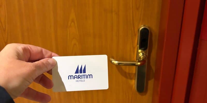 Eine Hand hält eine weiße Zimmerkarte des Maritim Hotels Hannover vor eine hölzerne Hotelzimmertür mit goldfarbenem Türgriff.