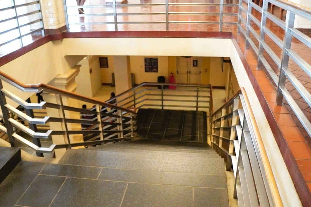 Blick von oben auf eine steinerne Treppe im Inneren des Ellis Island National Museum of Immigration in New York, die von Metallgeländern mit Holzhandläufen eingefasst ist.
