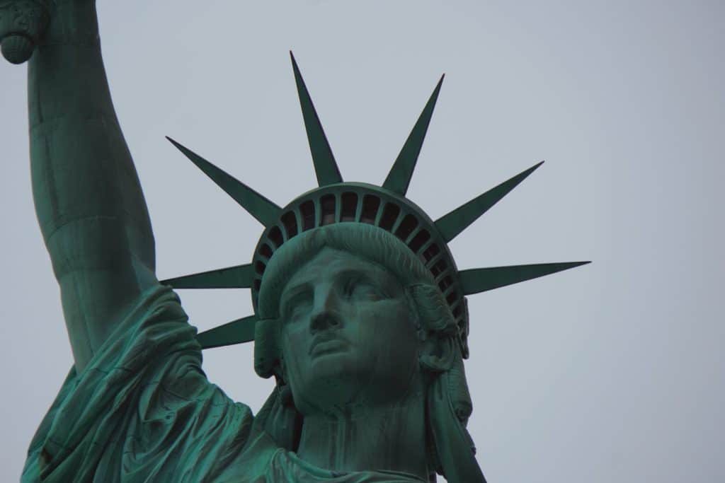 Nahaufnahme der Freiheitsstatue in New York, die ihren Kopf mit der markanten siebenstrahligen Krone und den erhobenen rechten Arm vor einem grauen Himmel zeigt.