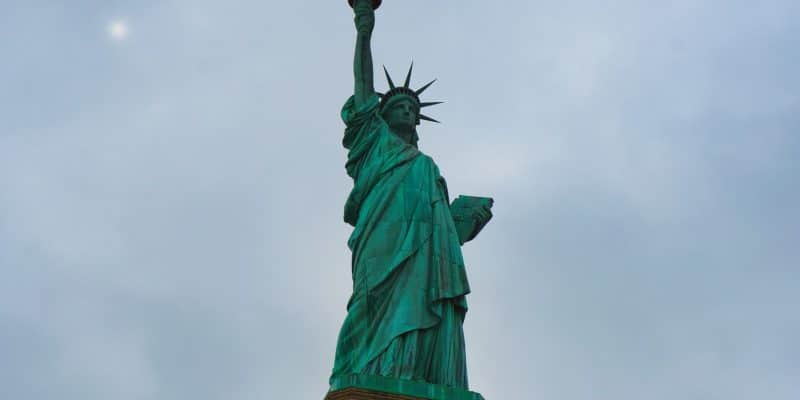 Die Freiheitsstatue in New York ragt vor einem bewölkten, grauen Himmel empor, während sie die Fackel hochhält und die Gesetzestafel im Arm trägt.