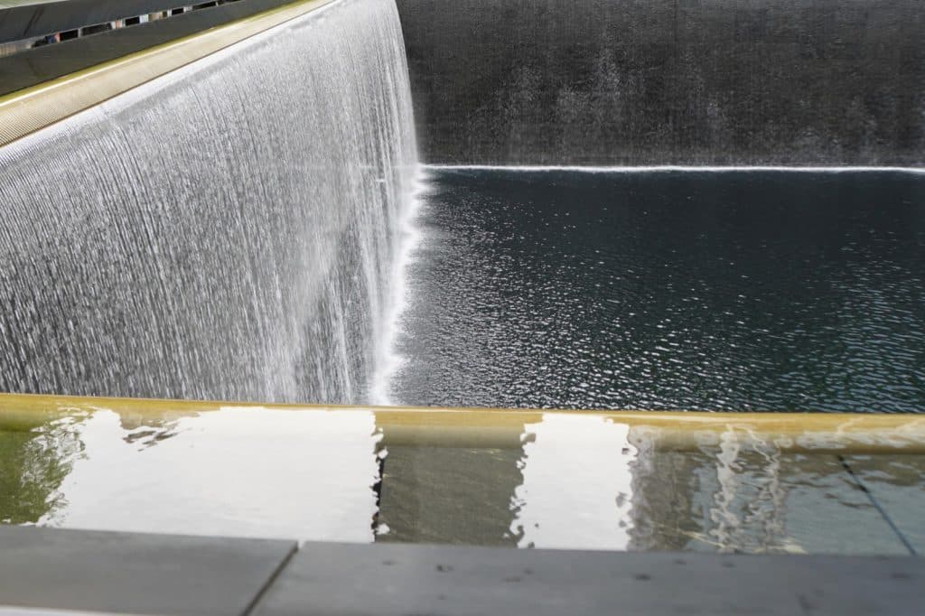 Nahaufnahme des National September 11 Memorial am Ground Zero in New York, das das rauschende Wasser zeigt, welches über die dunklen Wände in das tiefe Gedenkbecken stürzt.