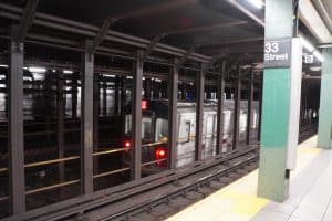 Ein New Yorker U-Bahn-Zug der Linie 4 fährt durch die Station 33rd Street, gesehen von einem Bahnsteig aus hinter stählernen Stützpfeilern.