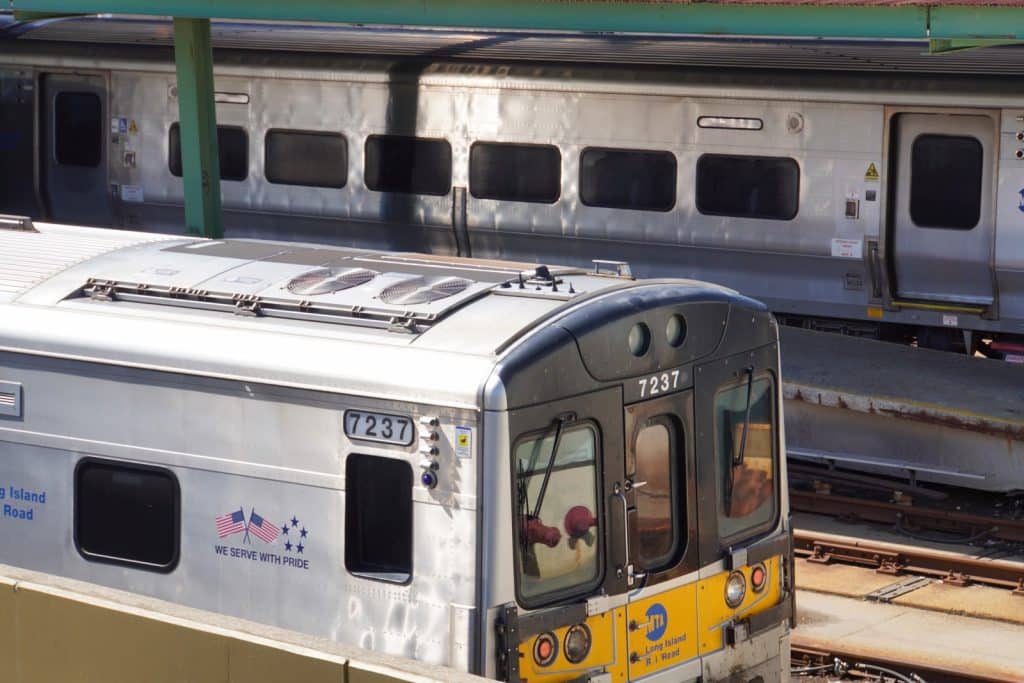 Nahaufnahme eines silbernen New York MTA Zuges der Long Island Rail Road mit der Nummer 7237, der neben einem weiteren Zug an einem Bahnsteig steht.