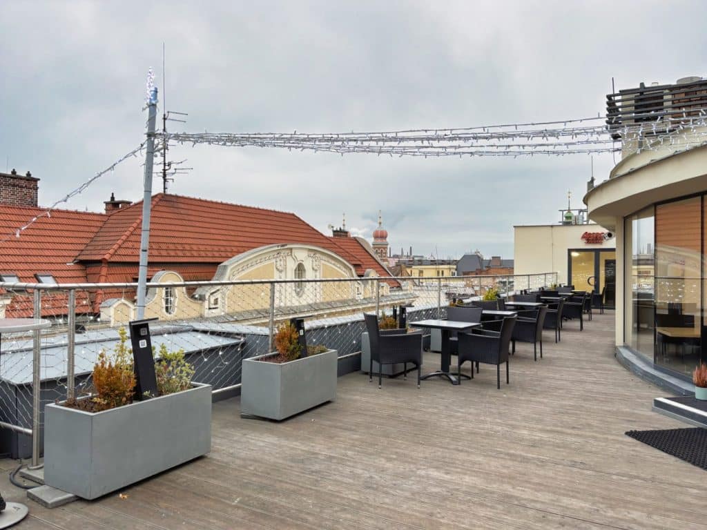 Dachterrasse des Hotel Central in Pilsen mit Holzboden, modernen Sitzgruppen und Pflanzkübeln vor dem Panorama der historischen Altstadt unter bewölktem Himmel.