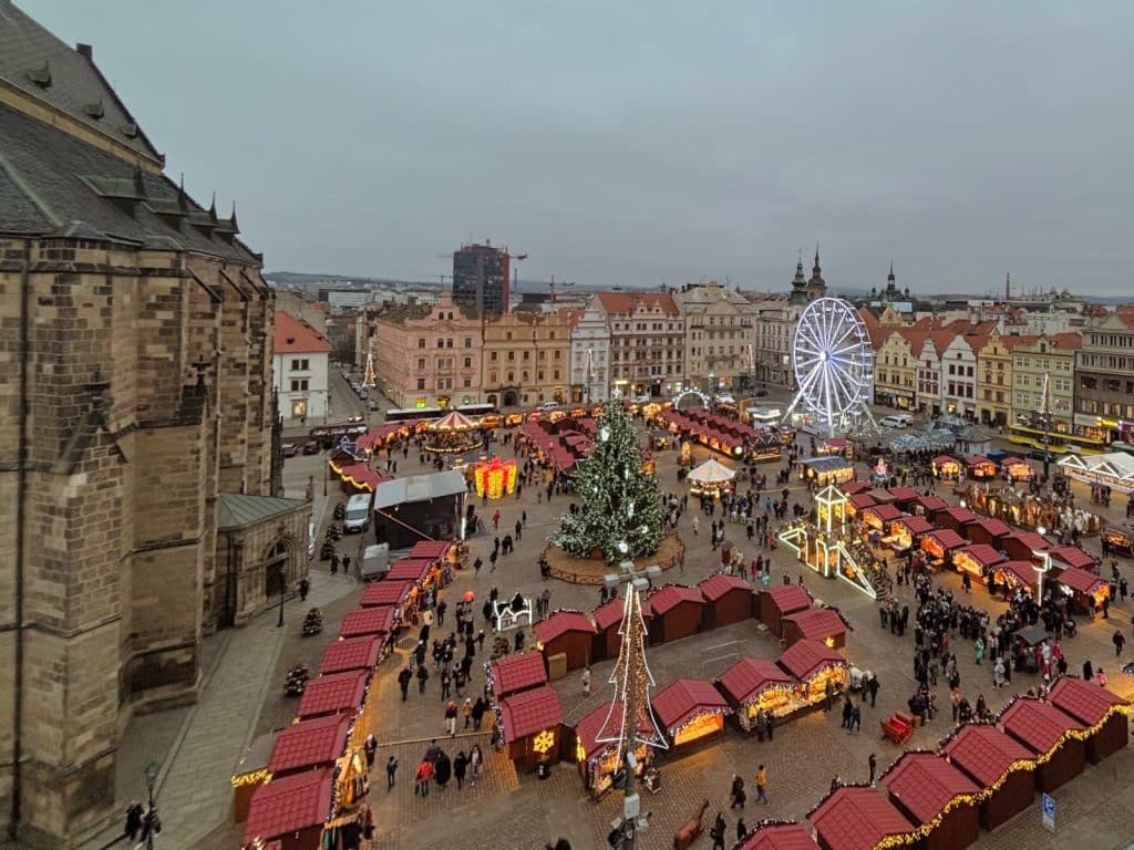 Blick von der Dachterrasse des Hotels Central auf den weihnachtlich beleuchteten Marktplatz von Pilsen mit zahlreichen Marktbuden, einem großen Weihnachtsbaum und einem Riesenrad vor historischer Kulisse.