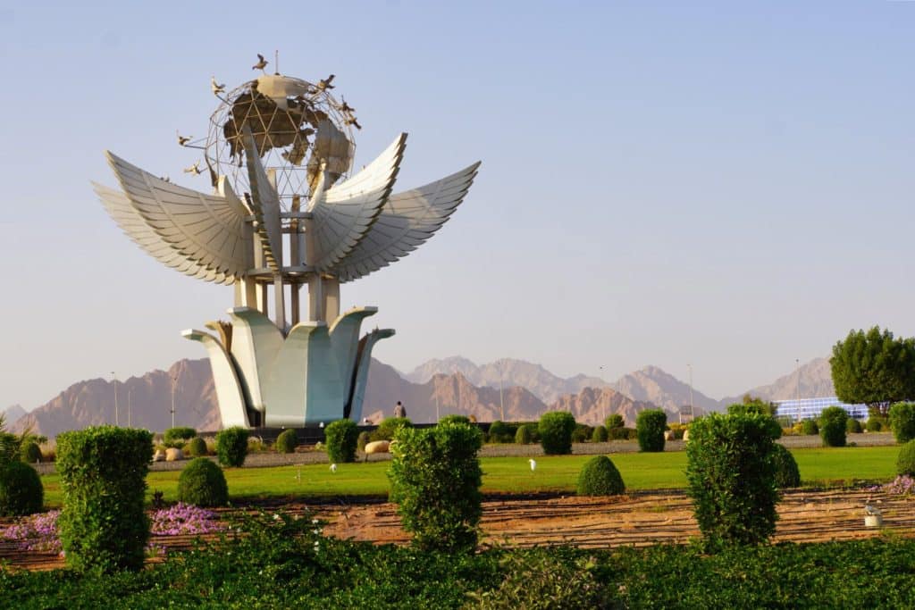 Sharm El Sheikh Sehenswürdigkeiten: Das Denkmal auf dem Friedensplatz zeigt eine monumentale Skulptur mit ausgebreiteten Flügeln, die einen Globus mit Tauben trägt, umgeben von gepflegten Grünanlagen vor einer Bergkulisse.