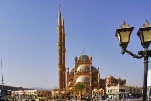 Die Al-Sahaba-Moschee in Sharm El Sheikh präsentiert sich mit ihrer kunstvollen Architektur aus sandfarbenem Stein, mehreren Kuppeln und zwei hoch aufragenden, schlanken Minaretten unter einem klaren blauen Himmel. Sharm El Sheikh Sehenswürdigkeiten