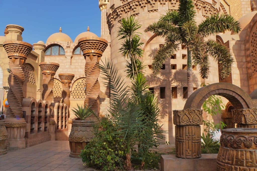 Seitenansicht des kunstvoll verzierten Eingangs der Al-Sahaba-Moschee in Sharm El Sheikh mit gedrehten Säulen, steinernen Torbögen und Palmen unter blauem Himmel.