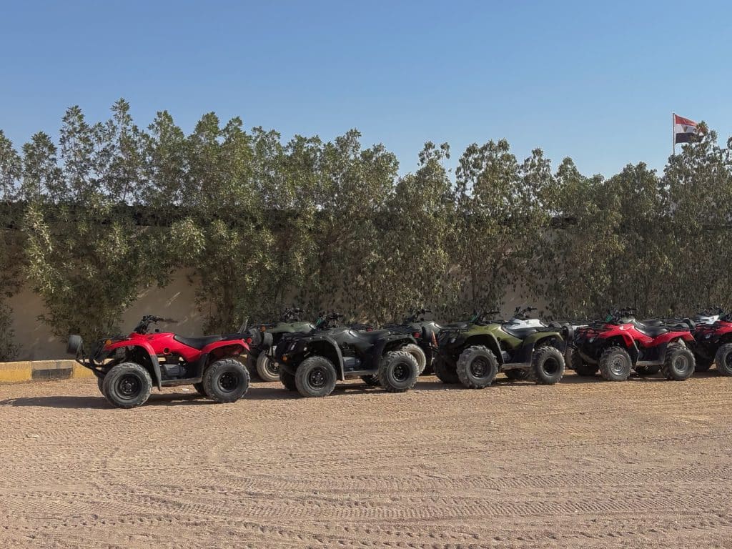Ausflugtipps Sharm El Sheikh: Eine Reihe von roten, schwarzen und grünen Quads steht an einem Startpunkt in Ägypten vor einer Baumreihe und einer ägyptischen Flagge bereit.