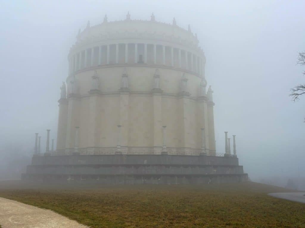 Die im dichten Nebel stehende Befreiungshalle in Kelheim präsentiert sich als monumentaler, runder Steinbau mit Säulengängen und Statuen auf einem grasbewachsenen Hügel.