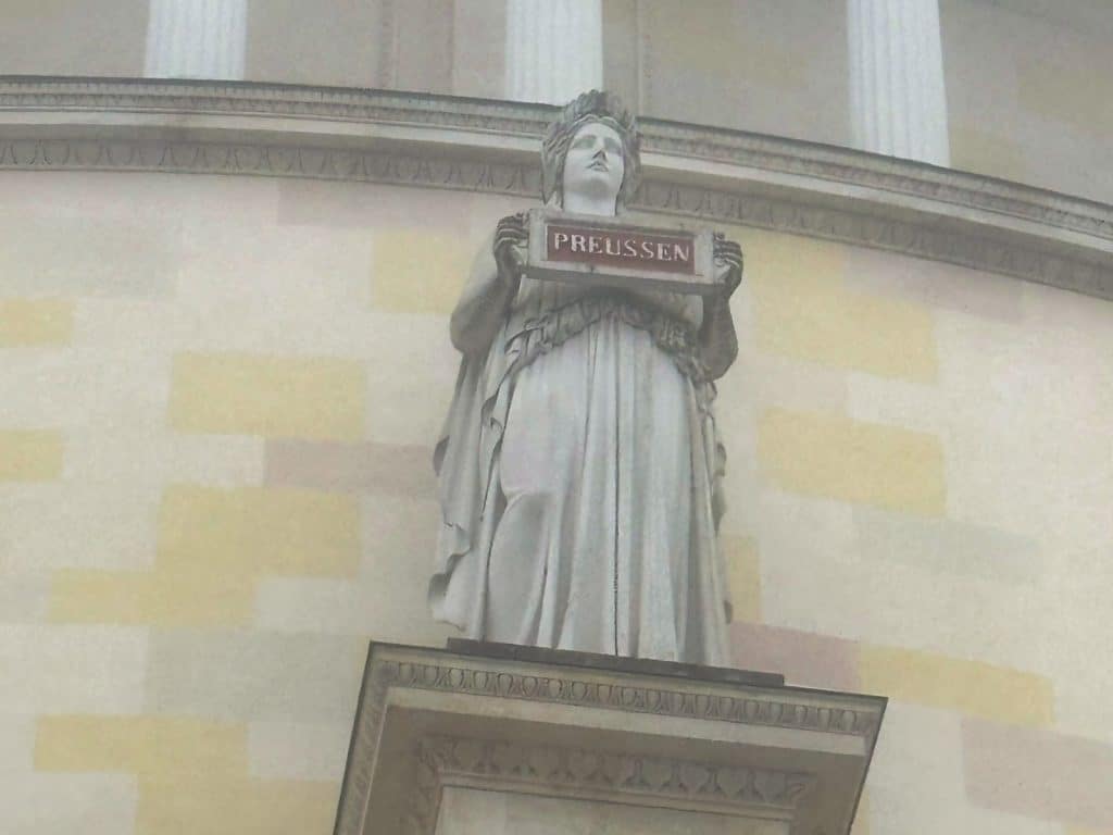 Eine Statue an der Außenfassade der Befreiungshalle in Kelheim stellt eine Frauengestalt in antikem Gewand dar, die eine Tafel mit der Aufschrift „PREUSSEN“ hält.
