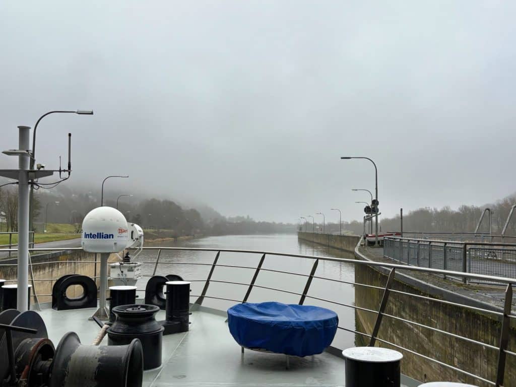 Blick vom Bug des Schiffes Belvedere auf die Einfahrt in eine Schleuse bei nebligem Wetter auf einem Fluss.