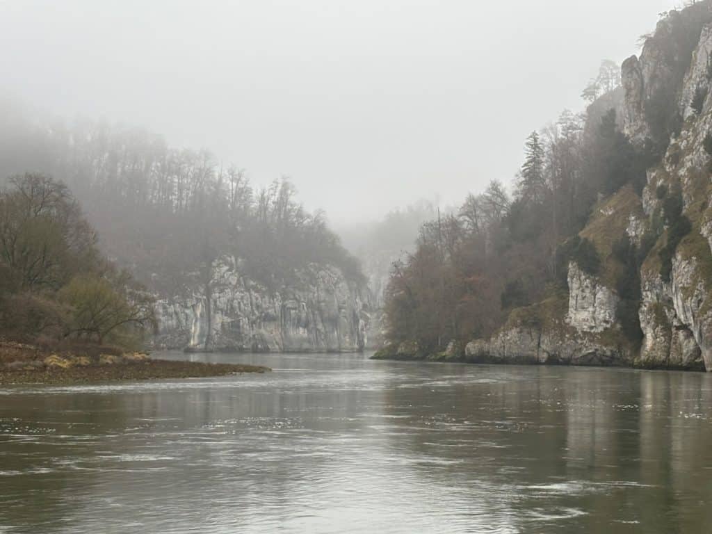 Blick auf den Donaudurchbruch bei Kelheim, wo der Fluss zwischen steilen, nebelverhangenen Kalkfelsen und bewaldeten Ufern fließt.