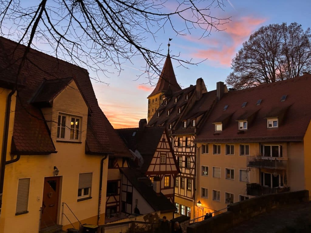 Blick über die Dächer der Nürnberger Altstadt mit ihren charakteristischen Fachwerkhäusern und einem spitzen Kirchturm vor einem farbenfrohen Abendhimmel in der Dämmerung.