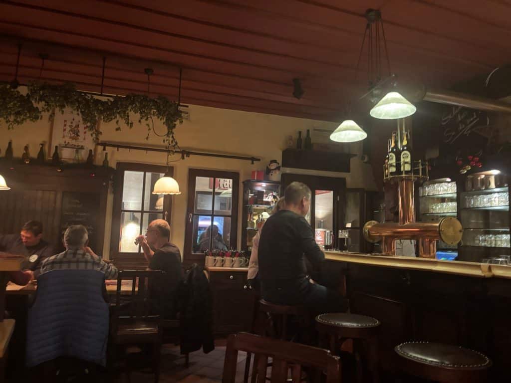 Innenansicht der Brauerei Altstadthof in Nürnberg mit Gästen, die an Holztischen und an der Bar unter warmem Licht in gemütlicher, rustikaler Atmosphäre sitzen.