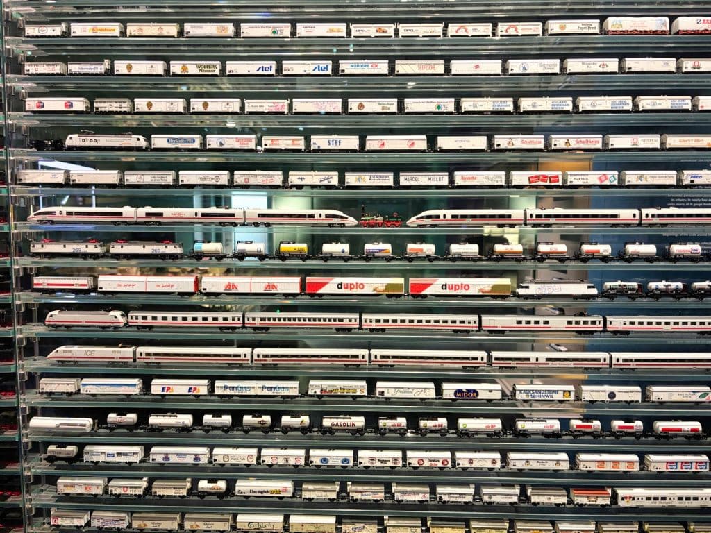 Zahlreiche Miniatur-Modelleisenbahnen und Waggons der Deutschen Bahn sind in einer beleuchteten Glasvitrine ordentlich in mehreren Reihen übereinander aufgereiht.