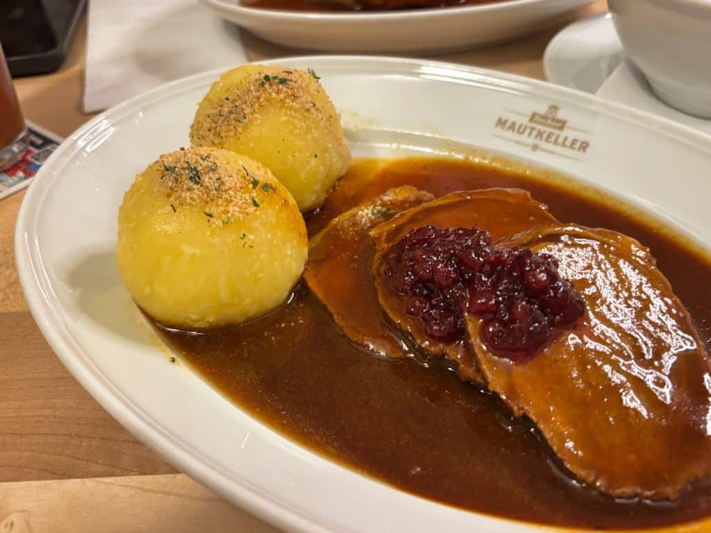 Ein klassischer Nürnberger Sauerbraten im Mautkeller, serviert mit zwei Kartoffelklößen in einer dunklen Bratensoße und garniert mit Preiselbeeren auf einem weißen Porzellanteller.