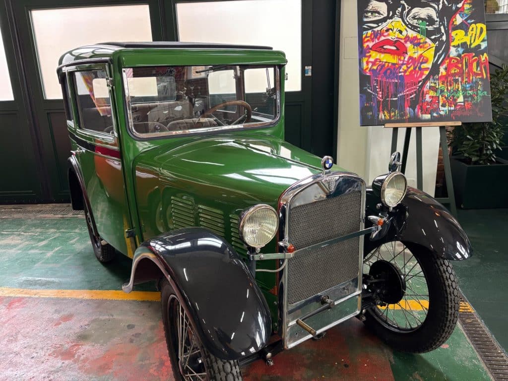 Ein historischer, grüner BMW 3/15 DA 2 aus der Pilsen Moto Art Kollektion neben einem modernen Pop-Art-Gemälde.