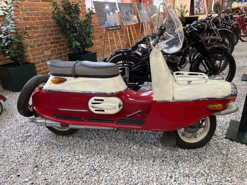 Ein rot-weißes Vintage-Motorrad der Marke Čezeta mit charakteristischer stromlinienförmiger Karosserie steht im Museum Pilsen Moto Art.