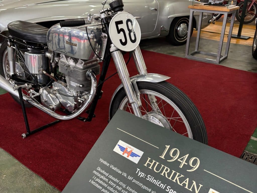 Ein silbernes Rennmotorrad der Marke Hurikan aus dem Jahr 1949 mit der Startnummer 58 steht in der Ausstellung Pilsen Moto Art vor einer Informationstafel.