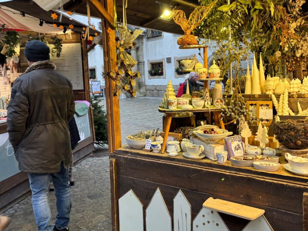 Ein Mann mit Winterjacke betrachtet einen festlich geschmückten Stand auf dem Lucrezia-Weihnachtsmarkt in Regensburg, der handgefertigte Keramik, Kerzen und weihnachtliche Dekorationen anbietet.
