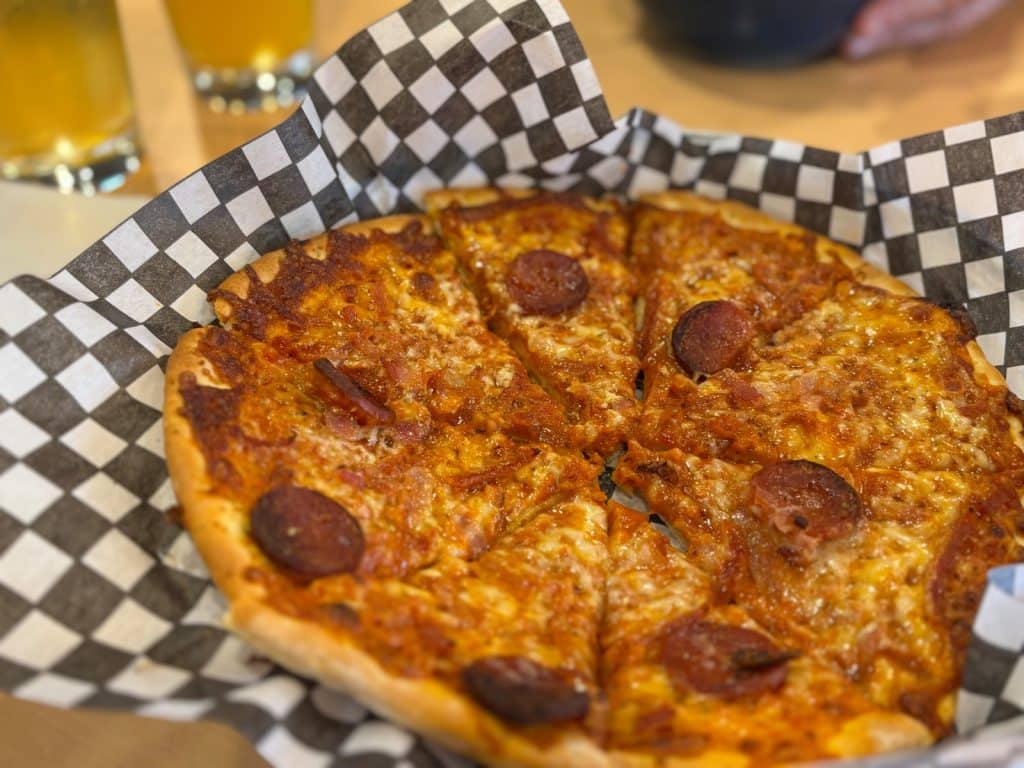 Eine frisch gebackene Pizza mit Salami und geschmolzenem Käse wird in einem Korb mit schwarz-weiß kariertem Papier in der Tadoussac Brauerei serviert.