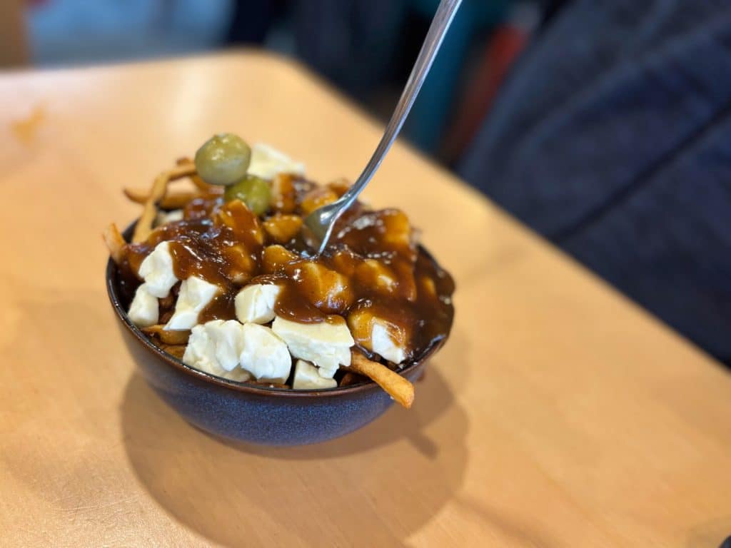 Eine Schüssel Poutine der Microbrasserie Tadoussac mit Pommes frites, frischen Käsequark-Stücken, brauner Bratensauce und zwei grünen Oliven als Garnitur.