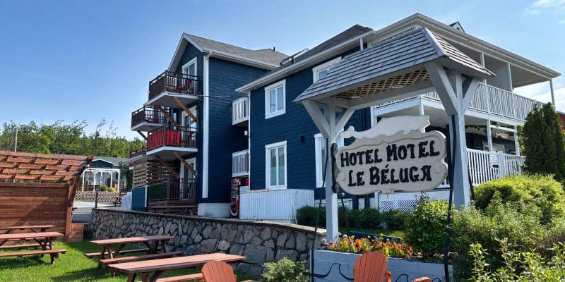 Das Hotel Motel Le Béluga in Tadoussac präsentiert sich als blaues, mehrstöckiges Gebäude mit weißen Balkonen, davor laden orangefarbene Stühle und Picknicktische auf einer Rasenfläche zum Verweilen ein.