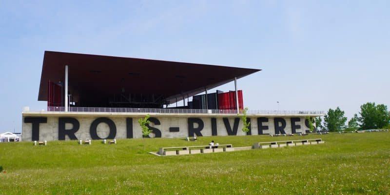 Das Amphithéâtre Cogeco in Trois-Rivières mit seinem markanten, flachen Dach und dem großen, schwarzen Schriftzug „TROIS-RIVIÈRES“ auf einer Betonmauer hinter einer grünen Wiese.