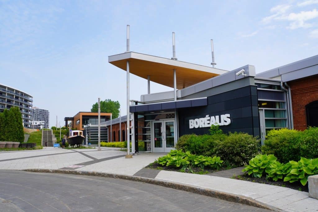 Außenansicht des Museums Boréalis in Trois-Rivières mit seinem modernen Eingangsbereich, einem markanten Vordach und einer gepflasterten Außenanlage unter blauem Himmel.