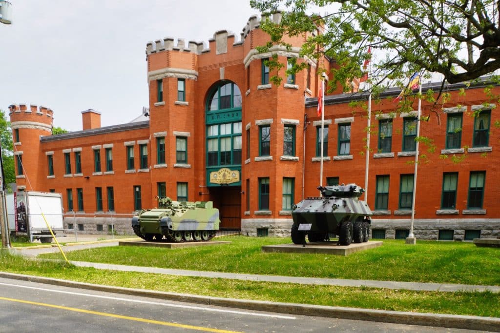 Sehenswürdigkeiten in Trois-Rivières: Das rote Backsteingebäude des Militärmuseums in Trois-Rivières ist im Festungsstil mit Zinnen erbau. Davor sind ein Kettenfahrzeug und ein Radpanzer auf dem Rasen ausgestellt.