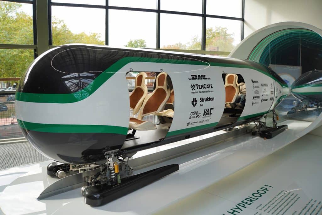 Ein futuristisches Modell einer Hyperloop-Kapsel mit weiß-grüner Lackierung und sichtbaren Sitzen im Innenraum ist im Eisenbahnmuseum in Utrecht vor einer Tunnelröhre ausgestellt.