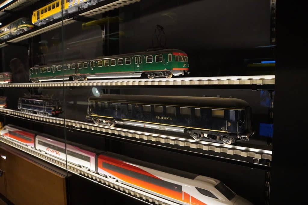 Verschiedene historische und moderne Eisenbahnmodelle, darunter ein grüner Triebwagen und ein Hochgeschwindigkeitszug, sind in einer beleuchteten Glasvitrine im Eisenbahnmuseum in Utrecht ausgestellt.