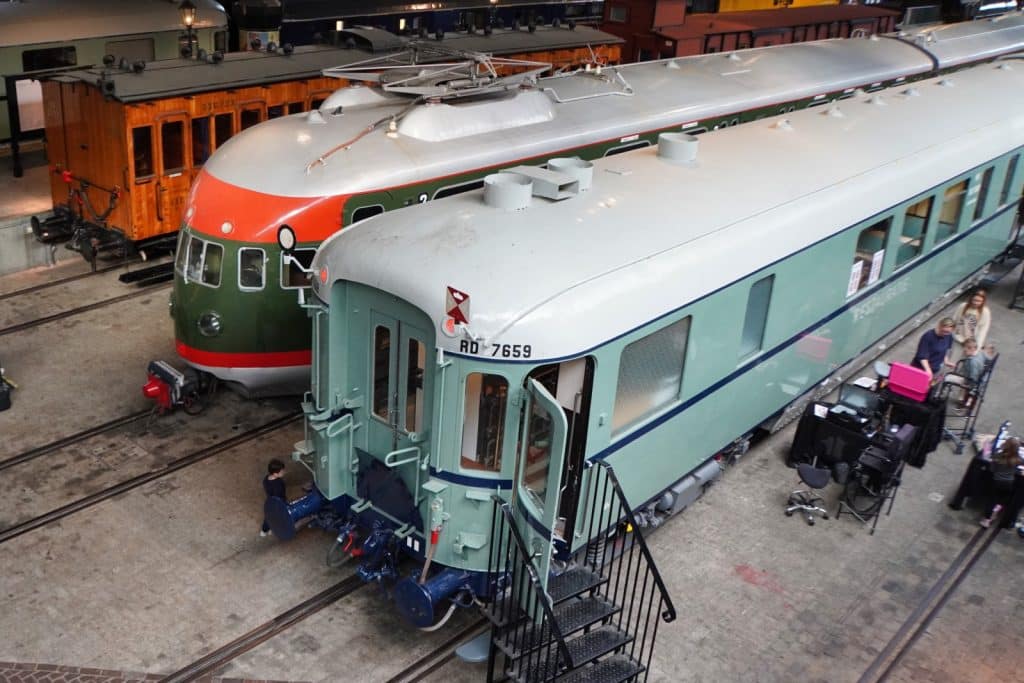 Blick von oben auf historische Züge im Eisenbahnmuseum in Utrecht, darunter ein grün-weißer Triebwagen mit roter Front und ein hellblauer Waggon mit der Aufschrift RD 7659.
