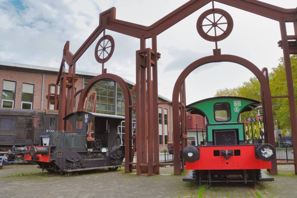 Zwei kleine historische Lokomotiven stehen vor einer rostfarbenen Stahlkonstruktion im Außenbereich des Eisenbahnmuseums in Utrecht.