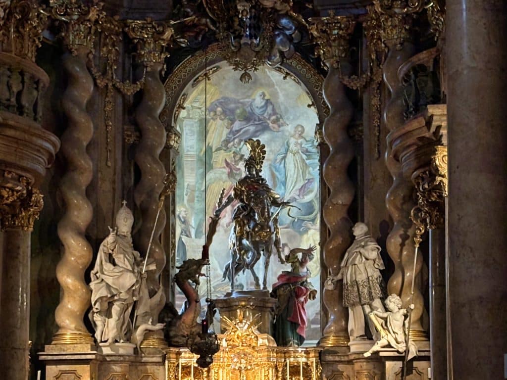 Der prunkvolle barocke Hochaltar der Klosterkirche Weltenburg zeigt eine zentrale Reiterstatue des Heiligen Georg im Kampf mit dem Drachen vor einem hellen Fresko, gerahmt von gewundenen Säulen und weißen Heiligenfiguren.