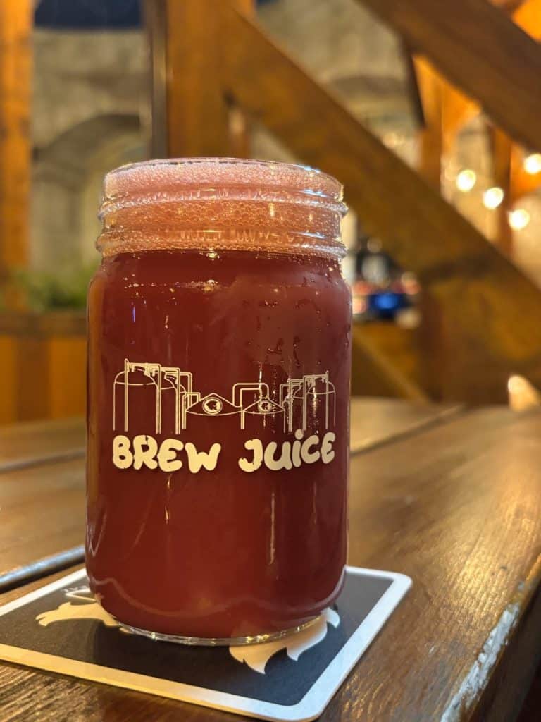 Brauerei im Vieux Port Montreal: Ein Glas Brewjuice der Brauerei Brewsky , gefüllt mit einem trüben, rötlichen Bier und einer feinen Schaumkrone, steht auf einem Untersetzer auf einem Holztisch.