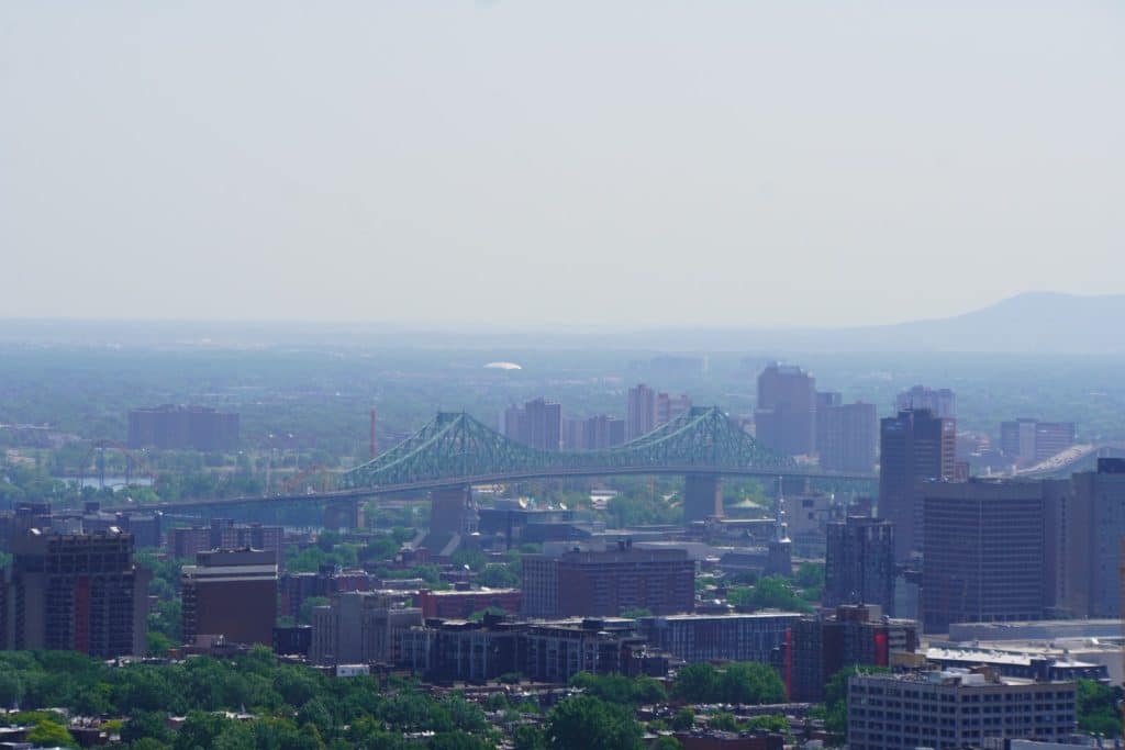 Blick vom Mont Royal über die Skyline von Montreal auf die markante grünliche Jacques-Cartier-Brücke, die den Sankt-Lorenz-Strom überquert.