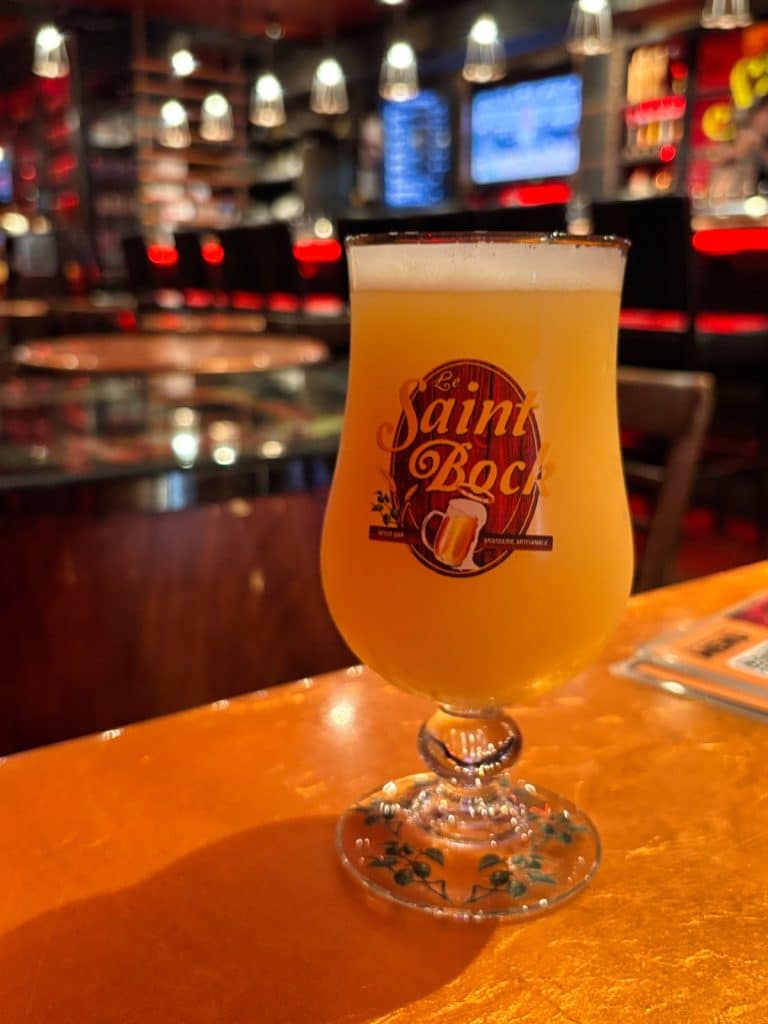 Ein Glas trübes IPA-Bier der Brasserie Le Saint-Bock steht auf einer hölzernen Theke in einer stimmungsvoll beleuchteten Bar in Montreal.