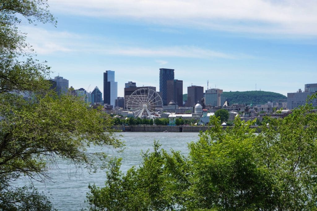 Blick über den Sankt-Lorenz-Strom auf die Skyline von Montreal mit dem markanten Riesenrad La Grande Roue de Montréal und dem Mont Royal im Hintergrund.