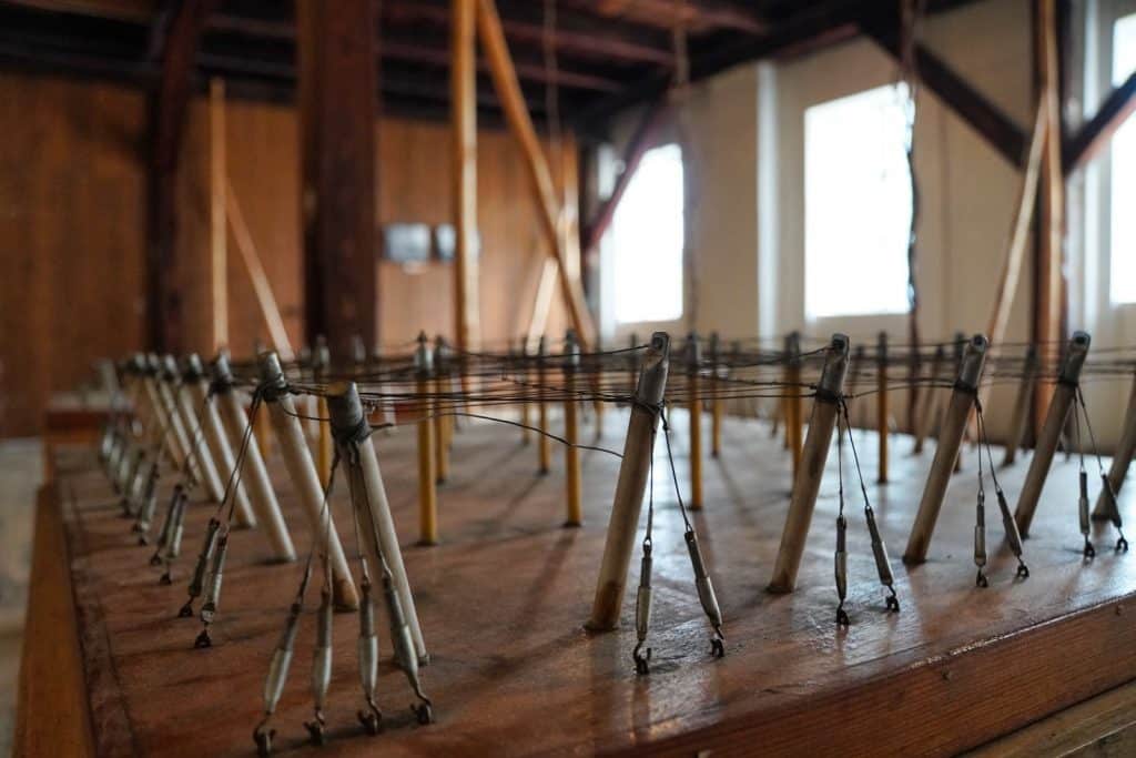 Ein hölzerner Nachbau eines Hopfenfeldes im Saazer Hopfenmuseum zeigt ein Miniaturmodell aus vertikalen Stäben und einem gespannten Drahtnetz in einem rustikalen Innenraum.