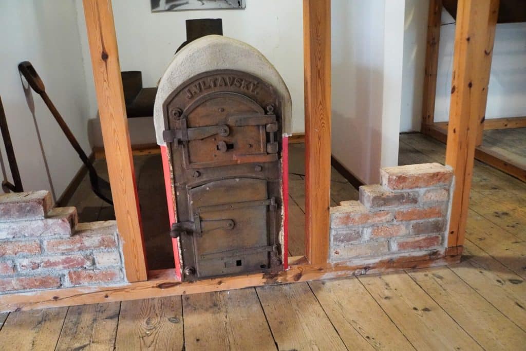 Ein historischer, gusseiserner Ofen mit der Aufschrift „J. VLTAVSKÝ“ steht in einer gemauerten Ziegelwand im Hopfenmuseum in Žatec (Saaz). Der Ofen befindet sich in einem Raum mit Holzboden und sichtbaren Balkenkonstruktionen.