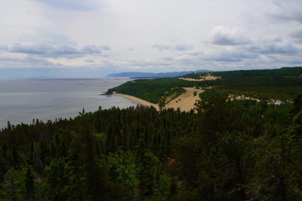 Blick von oben auf die bewaldete Küstenlandschaft von Tadoussac mit einer markanten Sanddüne, die zum Ufer des Sankt-Lorenz-Stroms hin abfällt.