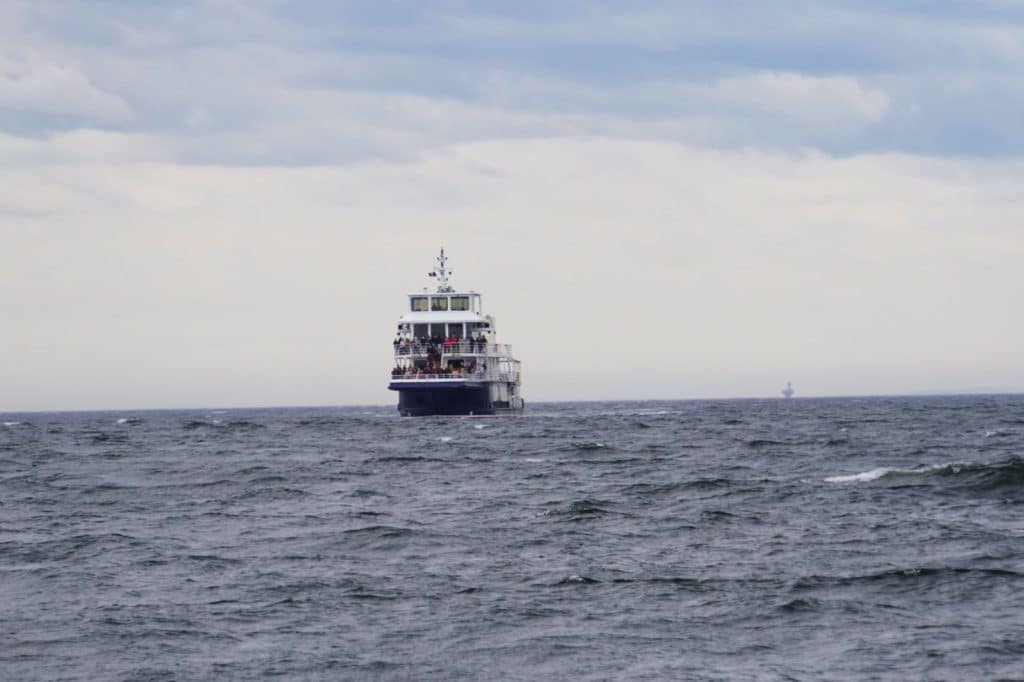 Ein großes, mehrstöckiges Ausflugsschiff für eine Waltour bei Tadoussac fährt auf dem weiten, leicht welligen Meer unter einem bewölkten Himmel.