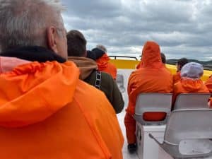 Passagiere in leuchtend orangefarbenen Regenjacken sitzen auf einem Zodiac-Boot während einer Waltour in Tadoussac unter einem bewölkten Himmel.